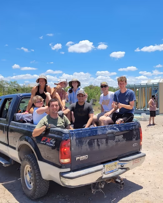 Group sitting in pickup truck bed under fluffy clouds on sunny day