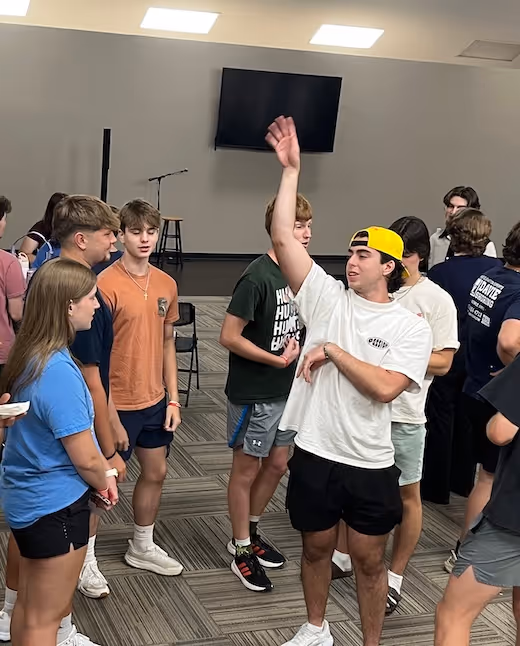 Group of teens standing together in a room, one raising hand