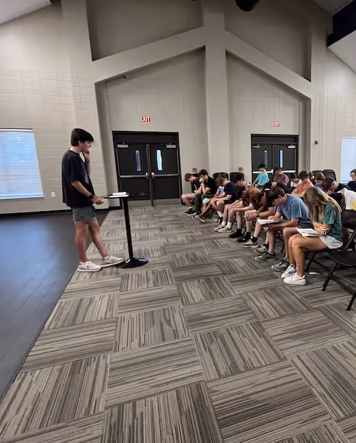 Student presents to seated audience in modern classroom with tiled floor