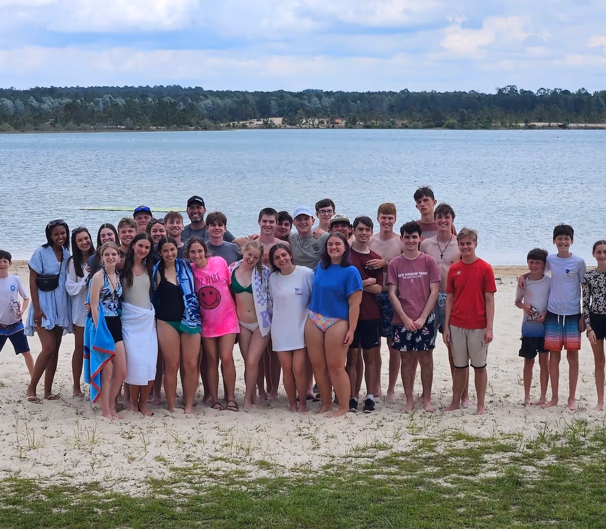 Large group of teens posing together on sandy beach by lake or river