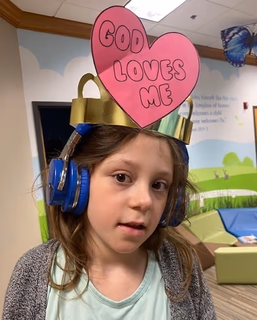Child wearing blue headphones with pink heart sign saying "God Loves Me"