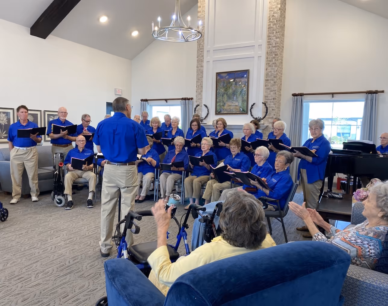 Senior choir in blue shirts performs for seated audience in community room