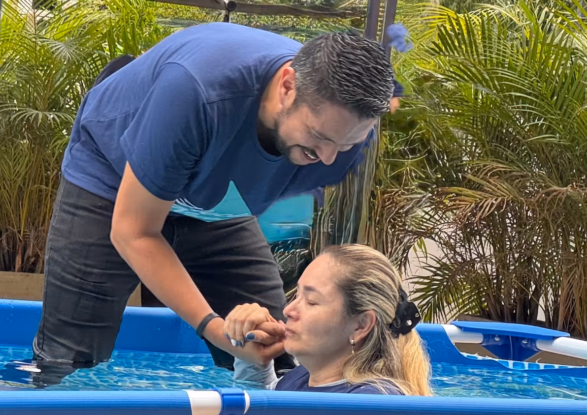 Baptism ceremony in a blue pool with palm trees in background