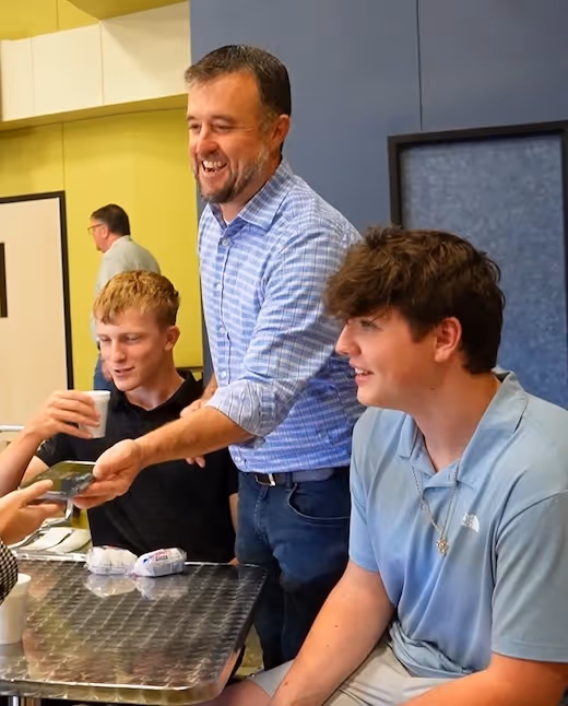 Smiling man serving drinks to two young people in a classroom