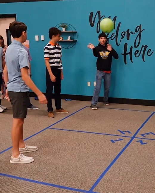 Students playing ball game on marked floor near teal wall with text
