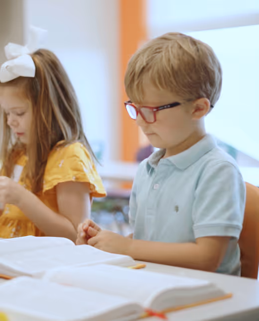 Two children studying at a table, one in yellow shirt, one in blue shirt