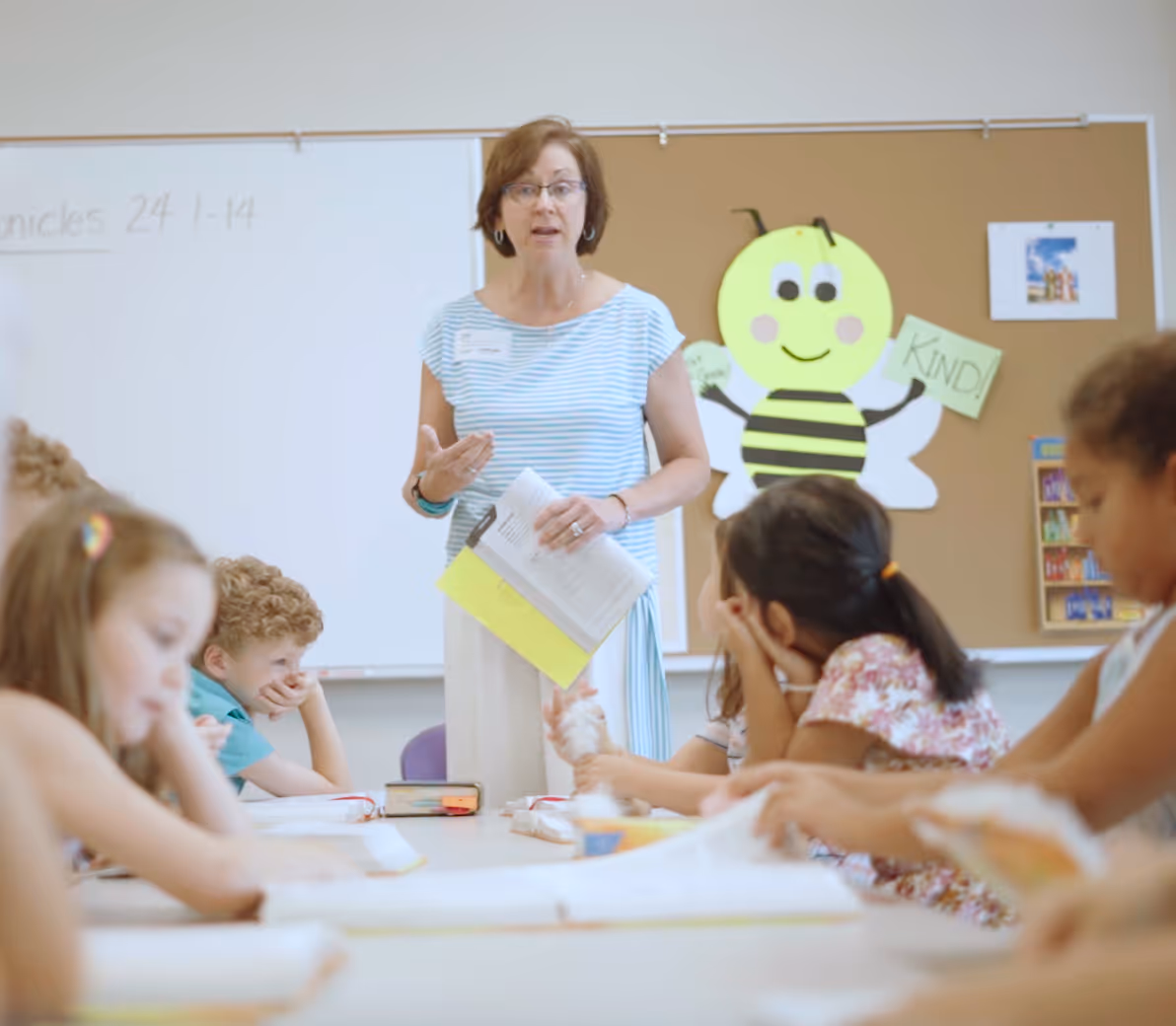 Teacher with yellow bee poster instructs students in elementary classroom