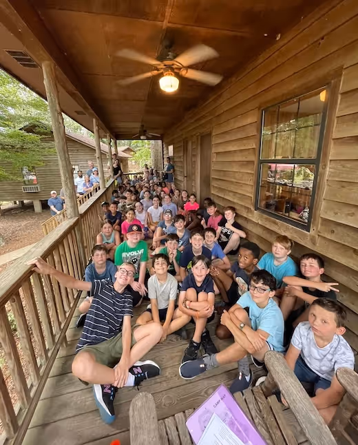 Large group of children sitting on wooden porch at summer camp
