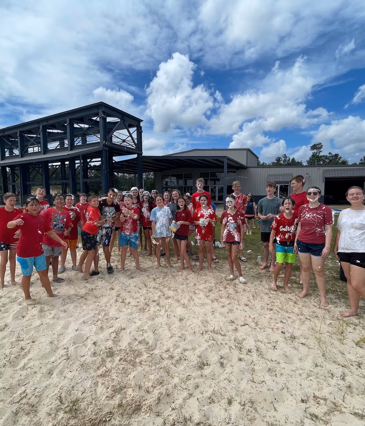 Large group of teens in red tie-dye shirts standing on sandy ground