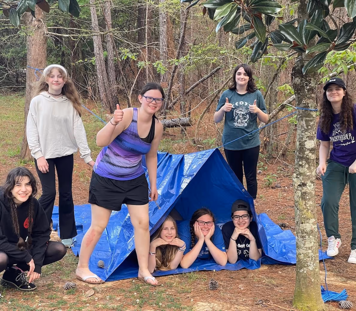 Group of young people posing around blue tent in forest campsite