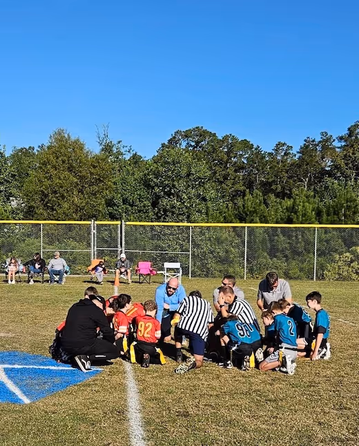 Youth football players and referees huddle on field during game break