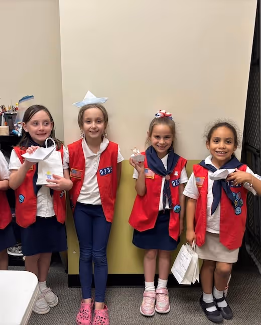 Four young students in red vests and badges smiling together
