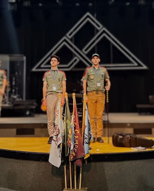 Two scouts standing on stage with national flags behind geometric backdrop