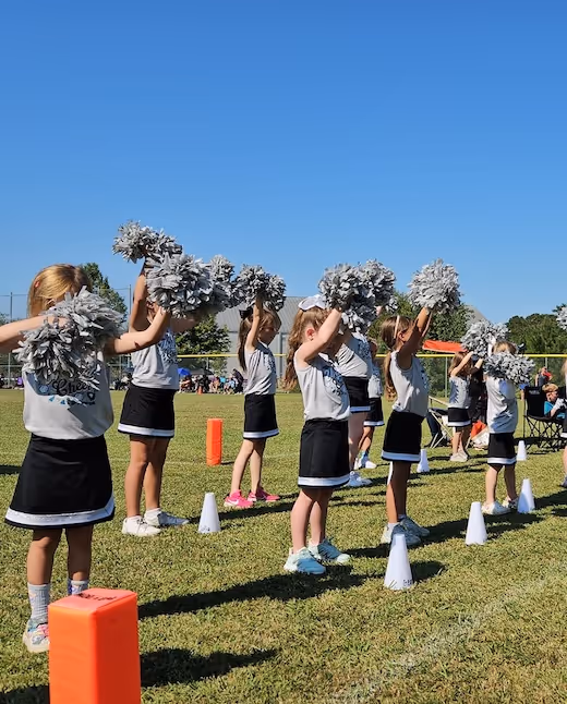 Young cheerleaders practice routine with pom-poms on sunny grass field
