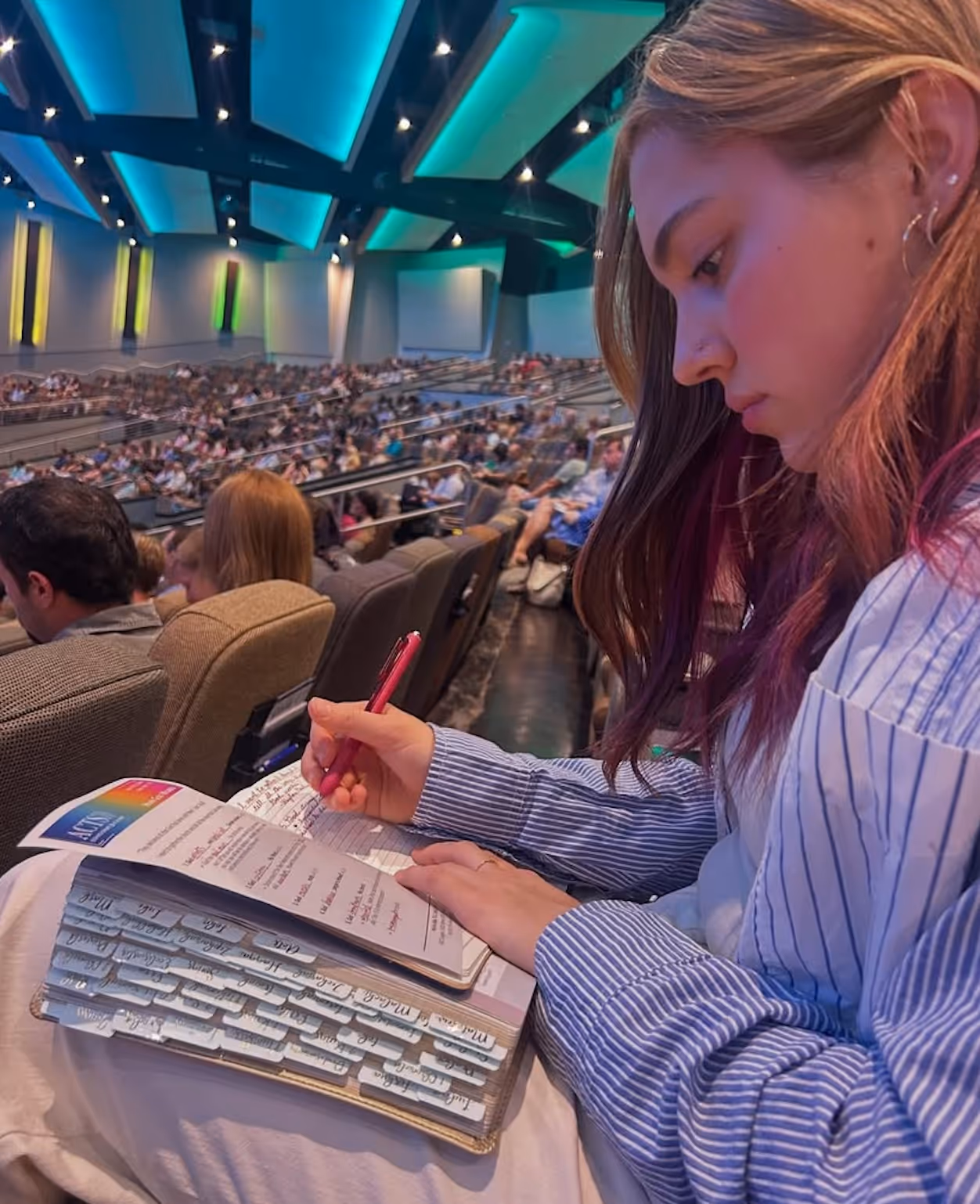 Woman taking notes during a lecture in a large auditorium with blue lighting