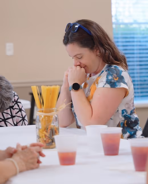 A woman praying at a table surrounded by other people at FBC Covington's Single Adults Ministry