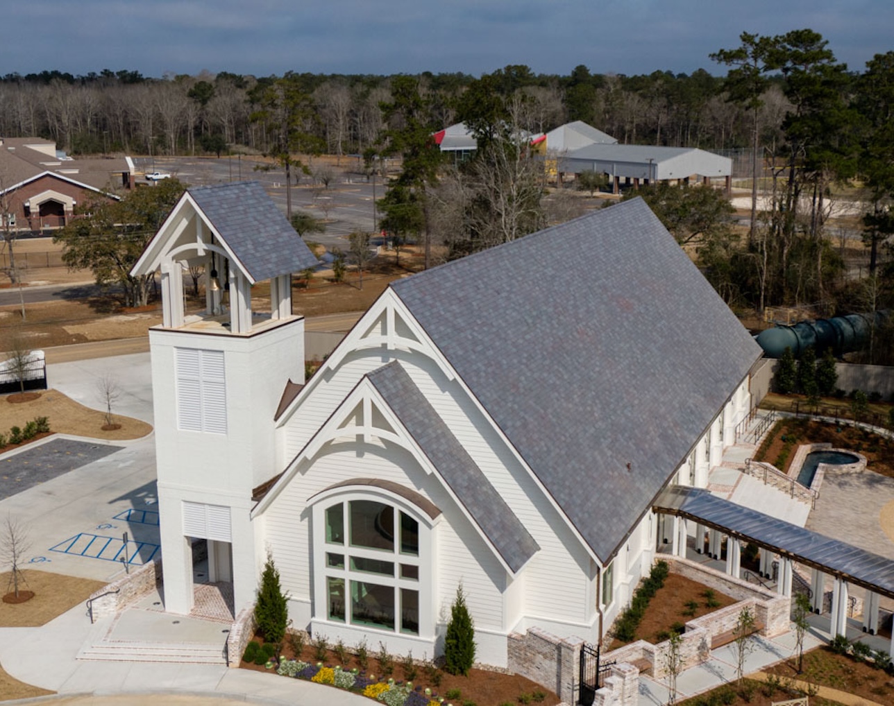 Aerial view of a white church building with a bell tower, large arched windows, and a covered walkway surrounded by landscaping.