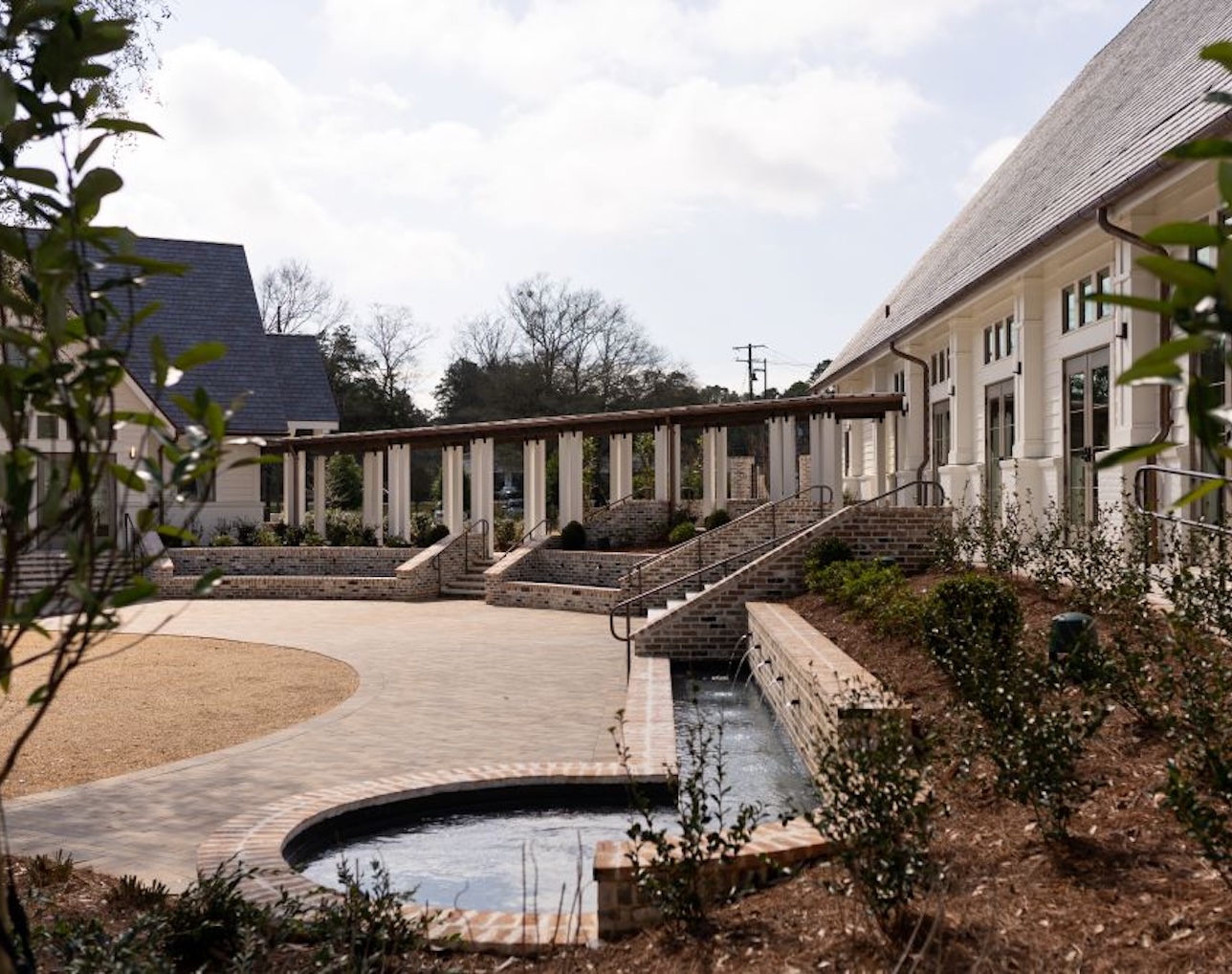 Outdoor courtyard with brick steps, a reflective pool, and white buildings with large windows under a partly cloudy sky.