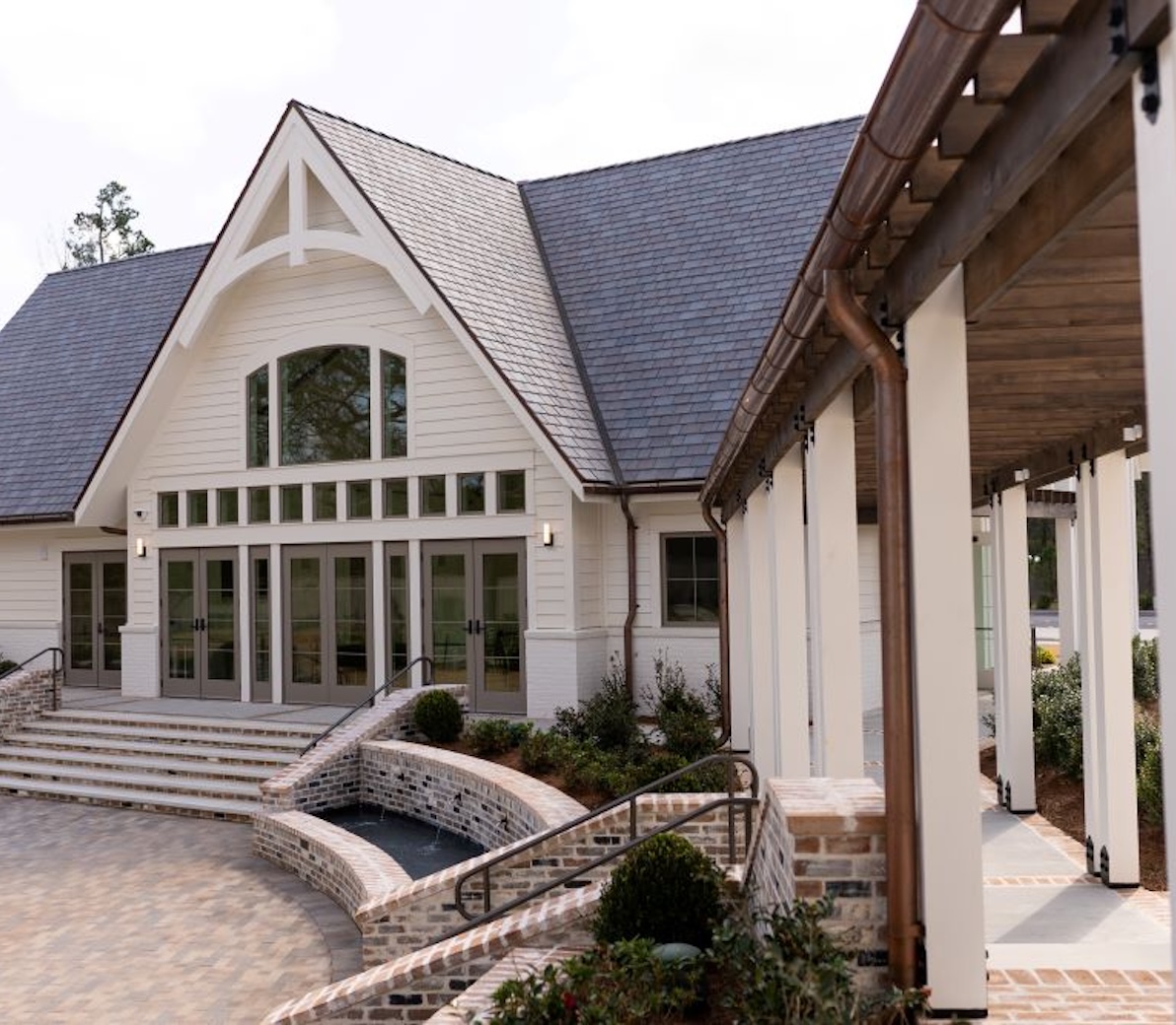 Modern building entrance with large glass doors, steps, brick planters, and a covered walkway with wooden ceiling.