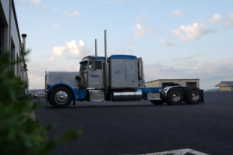 A semi-truck driving down a highway at dusk with headlights on