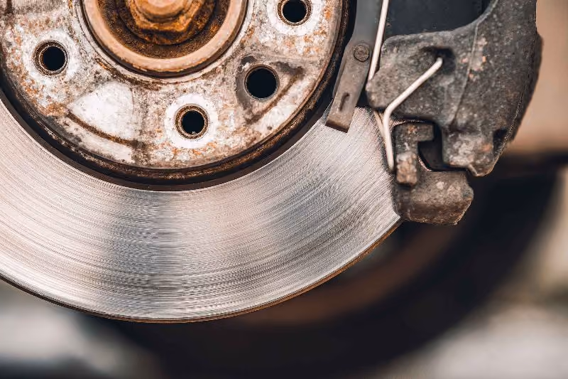 Close-up of worn vehicle brake rotor and caliper showing surface grooves, rusted hub, and braking components during automotive repair service