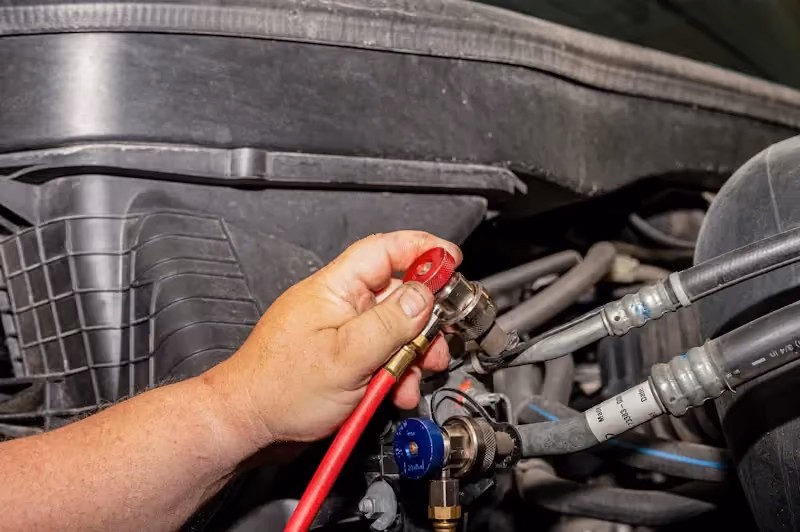 Truck HVAC service with a technician connecting A/C manifold gauges to diagnose and test the heavy-duty truck air conditioning system.