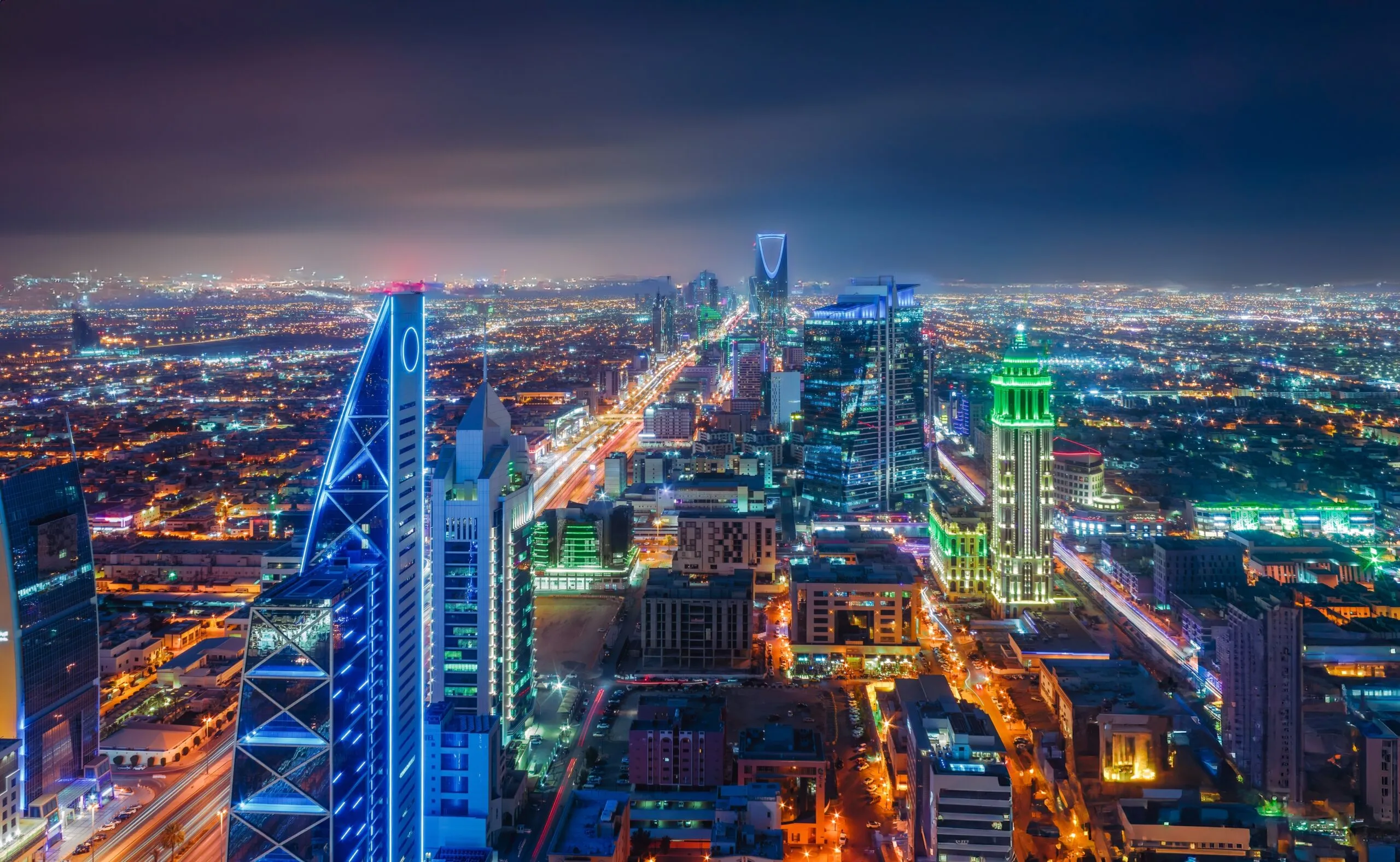 Nighttime cityscape with brightly lit skyscrapers and streets stretching into the distance under a dark sky.
