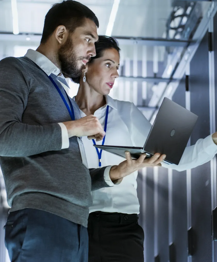 Man and woman wearing ID badges working together with a laptop in a server room.