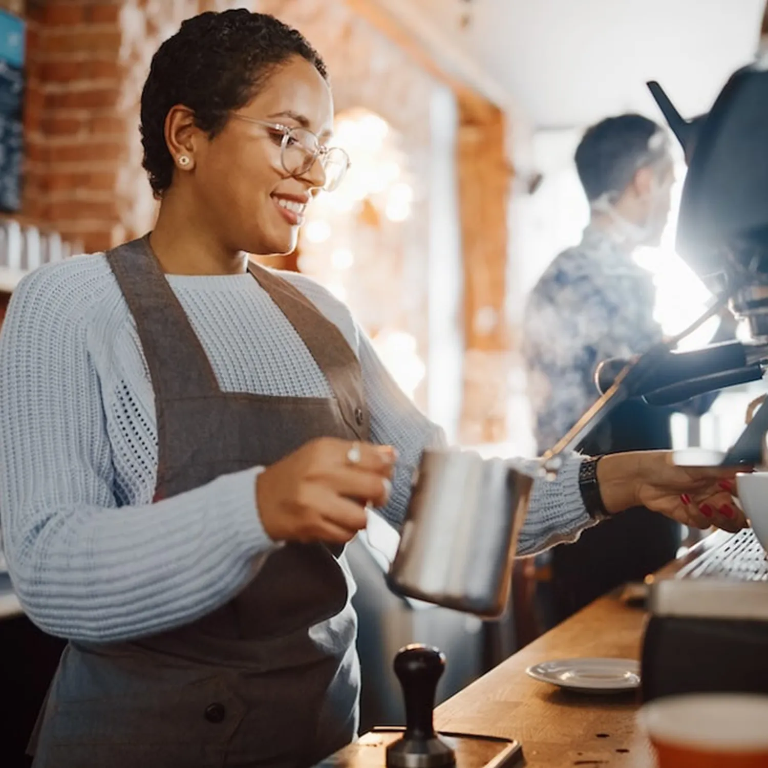 Smiling barista steaming milk with an espresso machine in a cozy coffee shop.