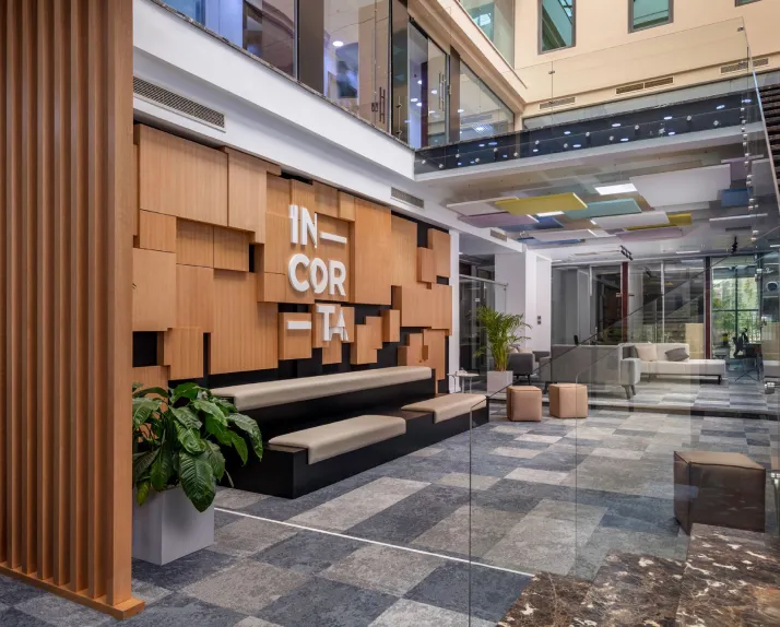 Modern Incorta office lobby with geometric wood wall design, branded Incorta signage, built-in seating, glass walls, and natural light from upper-level windows.