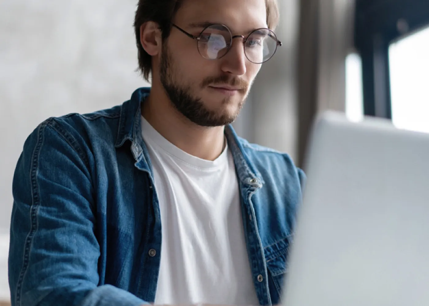 Focused young professional wearing glasses and working on a laptop in a modern office setting