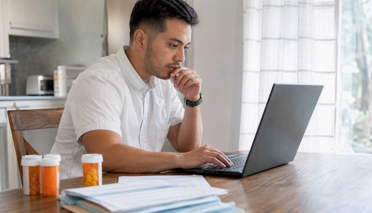 Hands typing on laptop with prescription documents nearby
