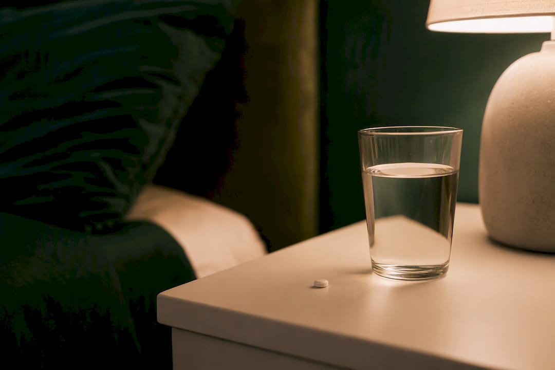 Pill and water glass on bedside table at night