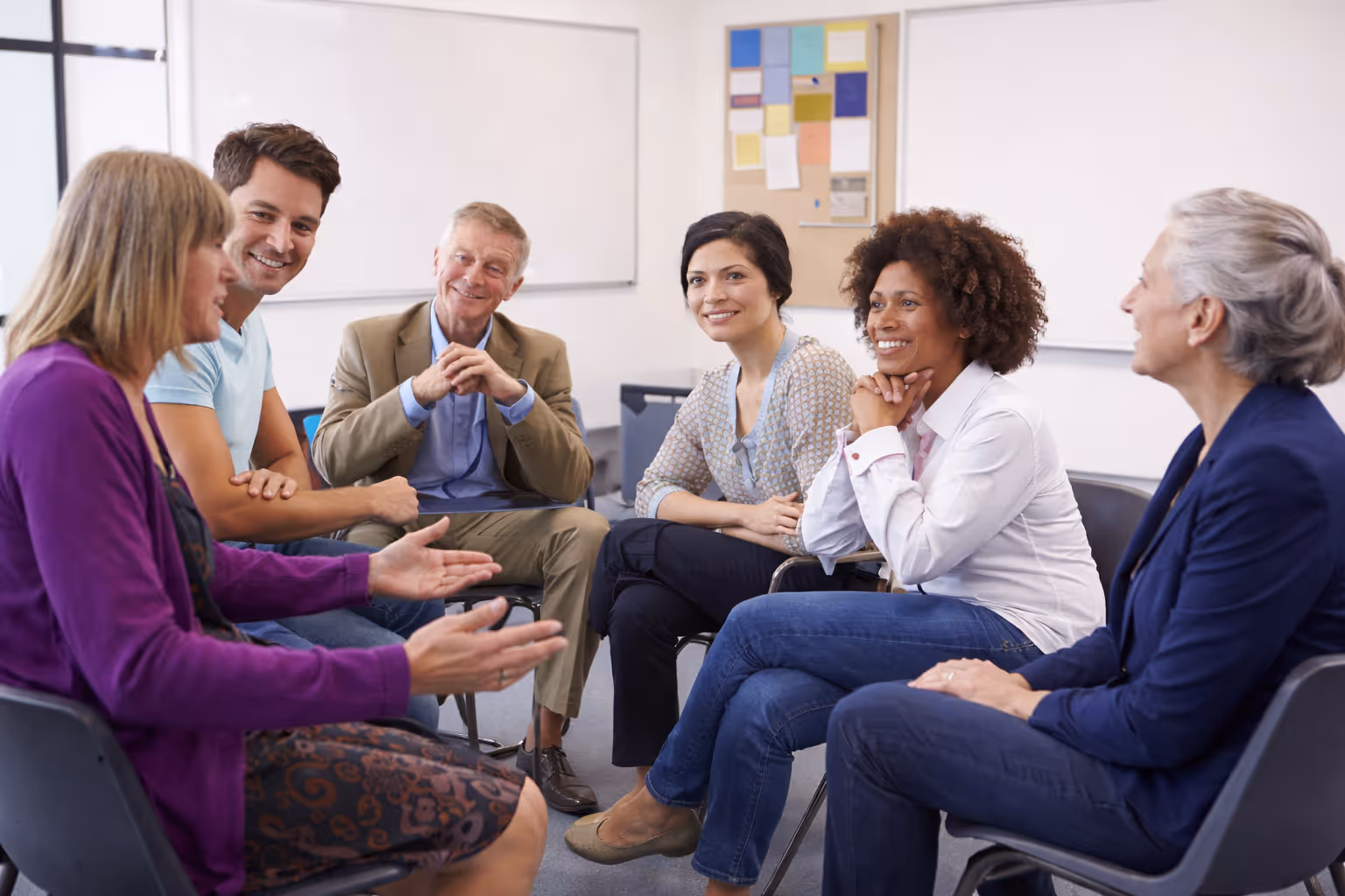 A teacher assists a group of diverse students using tablets in a bright classroom.