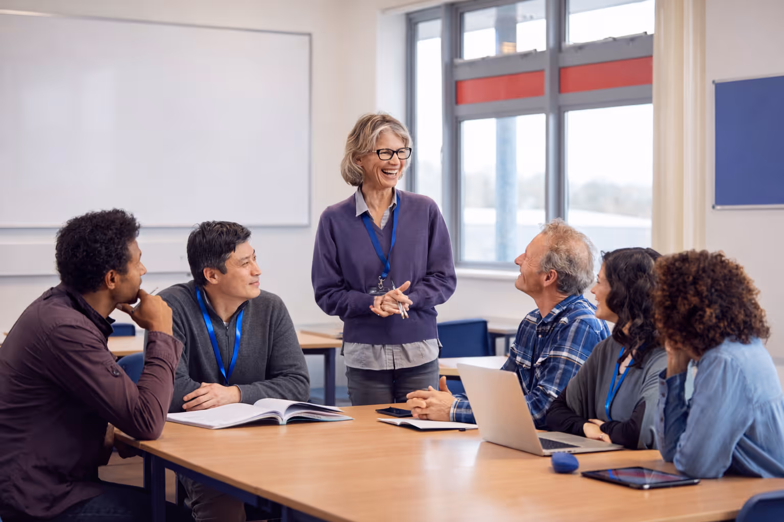 A teacher assists a group of diverse students using tablets in a bright classroom.