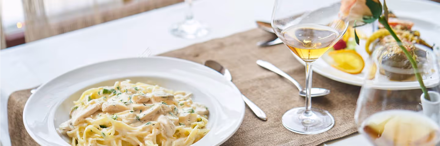 A table setting with a plate of pasta and a glass of white wine.