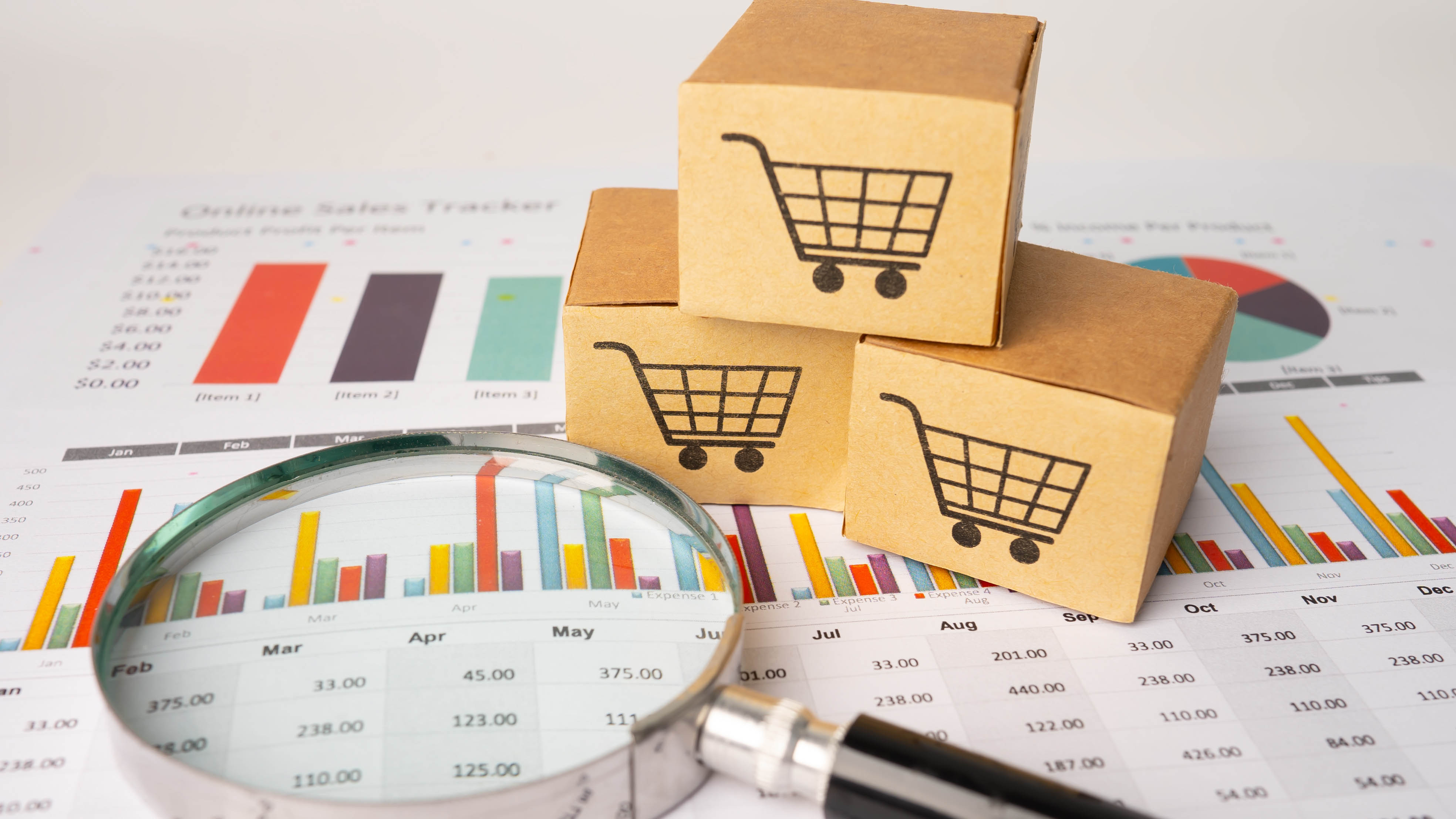 Shopping cart boxes and a magnifying glass resting on a printed sales analytics chart