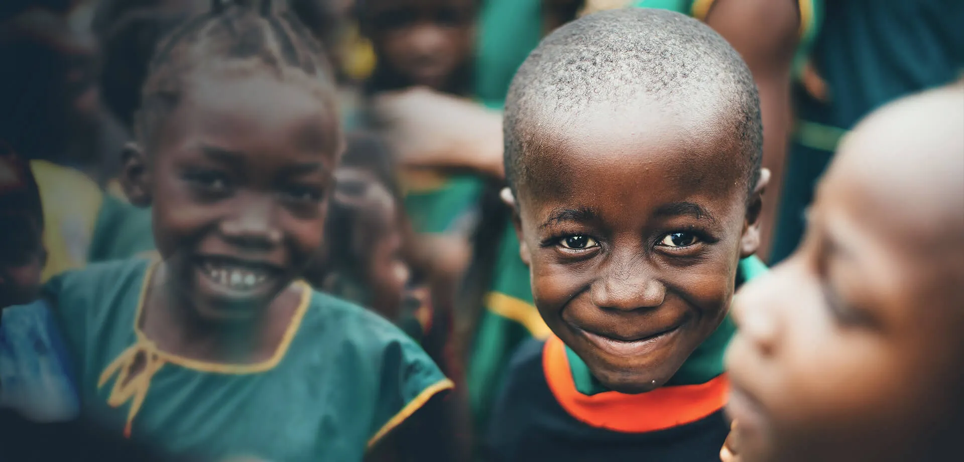 Zbliżenie uśmiechniętego młodego chłopca w kolorowych ubraniach z innymi dziećmi rozmytymi w tle.