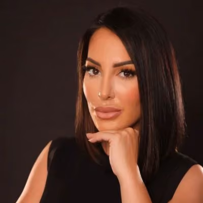 Woman with straight shoulder-length dark hair resting chin on hand against a dark background.