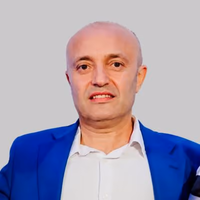 Portrait of a bald man wearing a blue blazer and white shirt against a gray background.