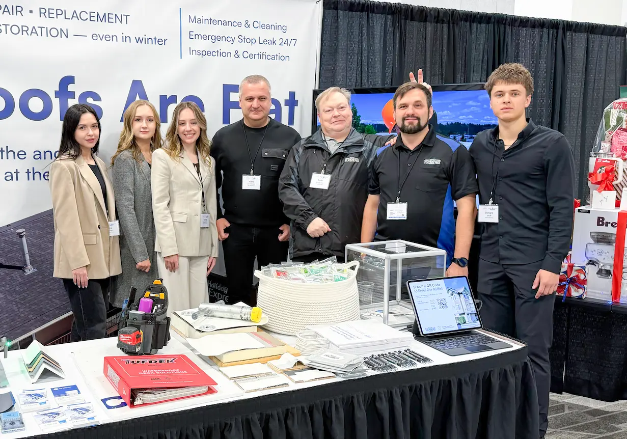 Group of seven people, team Flat Roof Pros, Inc standing behind a table with promotional materials and a laptop at a trade show booth.