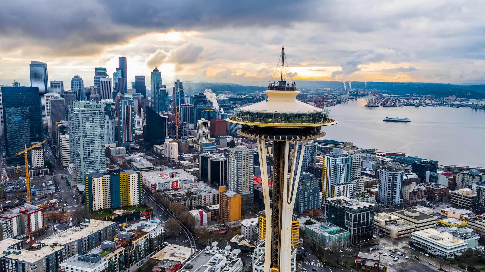 Aerial view of Seattle skyline with the Space Needle in the foreground and Elliott Bay in the background under a cloudy sky.