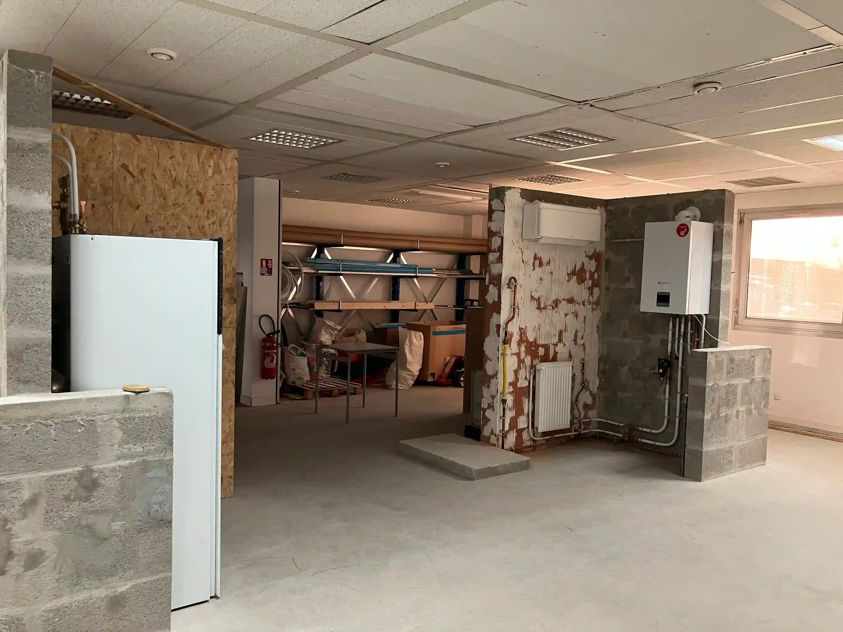Vue d'un plateau technique de formation en plomberie-chauffage, avec des installations de pompe à chaleur, de chauffage et de réseaux de tuyauterie sur des murs en parpaing dédiés à la pratique des étudiants.