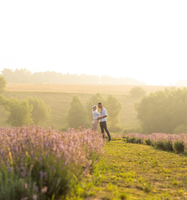 Koppel dat hand in hand loopt in een veld met paarse bloemen bij zonsondergang.