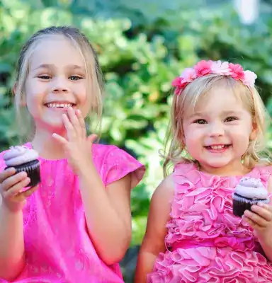 Twee schattige meisjes in het rose die een cupcake eten op een communie