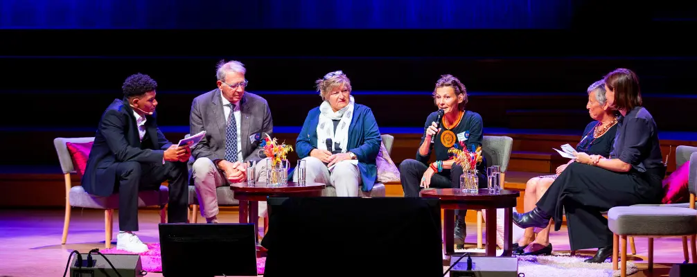 Vijf sprekers die op een podium zitten tijdens een professioneel congres