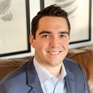 Smiling man in a blue blazer sitting on a leather couch, professional headshot.