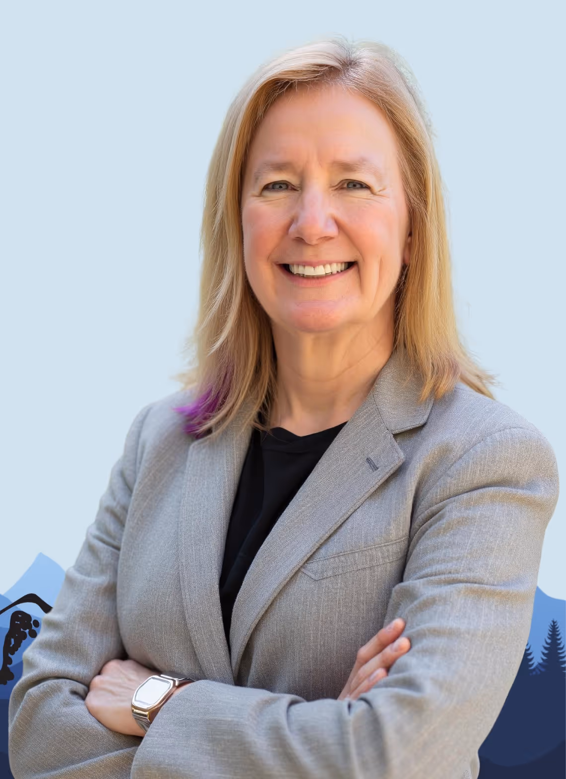 Smiling middle-aged woman with blonde hair in a gray blazer and black shirt standing with arms crossed.