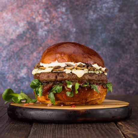 Burger artizanal cu brânză blue, carne de vită suculentă, ciuperci și salată proaspătă, servit pe un blat pufos. Disponibil la Stef’s Burgers.