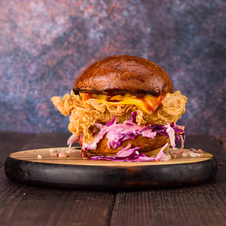 Burger cu pui crispy auriu, brânză cheddar topită, salată coleslaw crocantă și sos BBQ servit pe o chiflă pufoasă.
